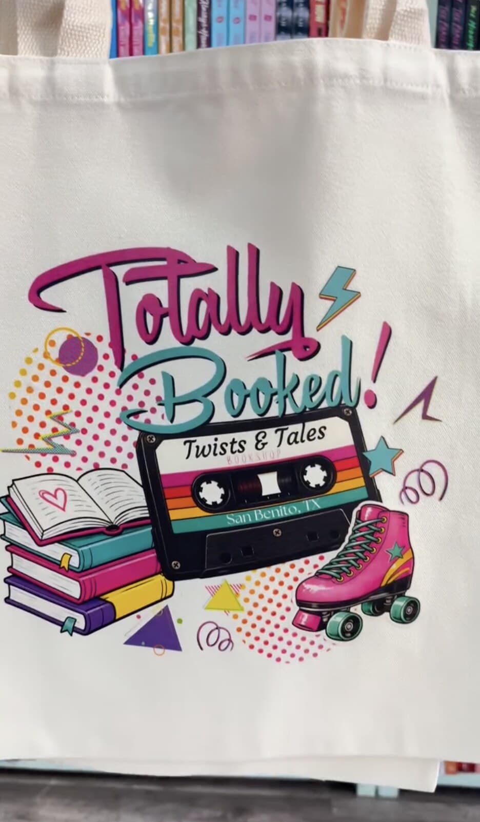 A Totally Booked Twists & Tales tote featuring colorful books, a cassette tape, and a roller skate.